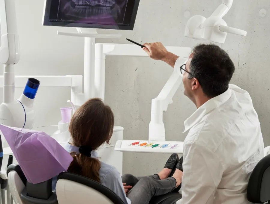 Dentist explaining dental x-ray to patient in modern clinic using screen display.