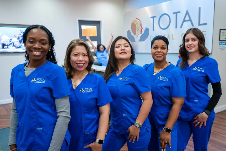 Diverse dental care team in blue scrubs smiling confidently inside Total Dental Care clinic.