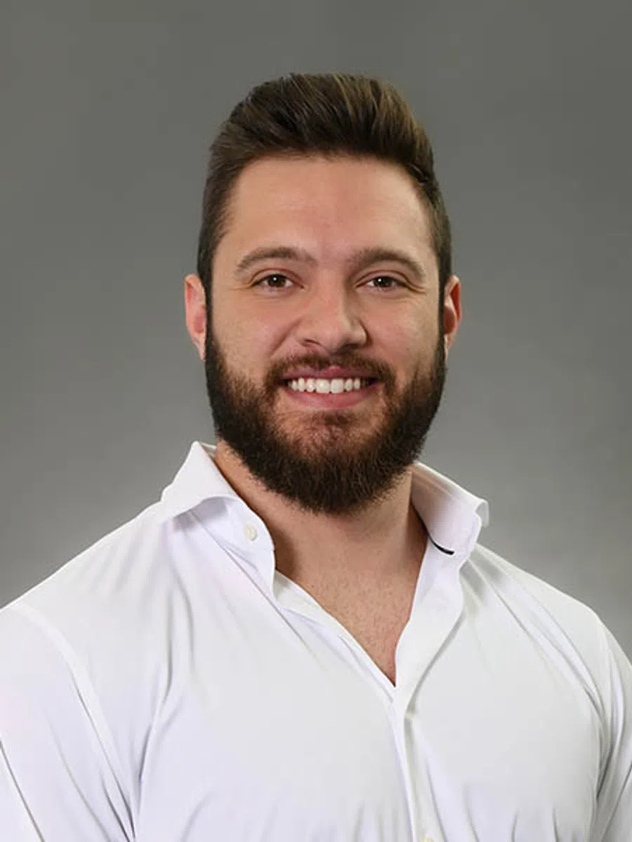 Smiling young man with beard wearing a white button-up shirt against a gray background