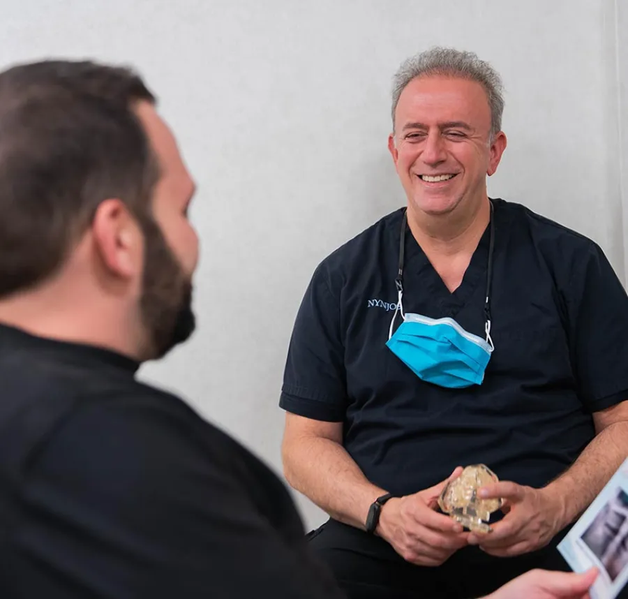 Smiling doctor in black scrubs discussing dental model with patient in consultation room
