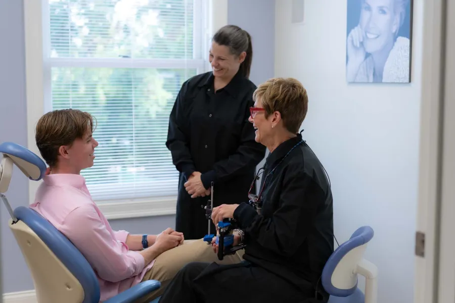 Dental patient in pink shirt consults with two female dental professionals in bright office room.