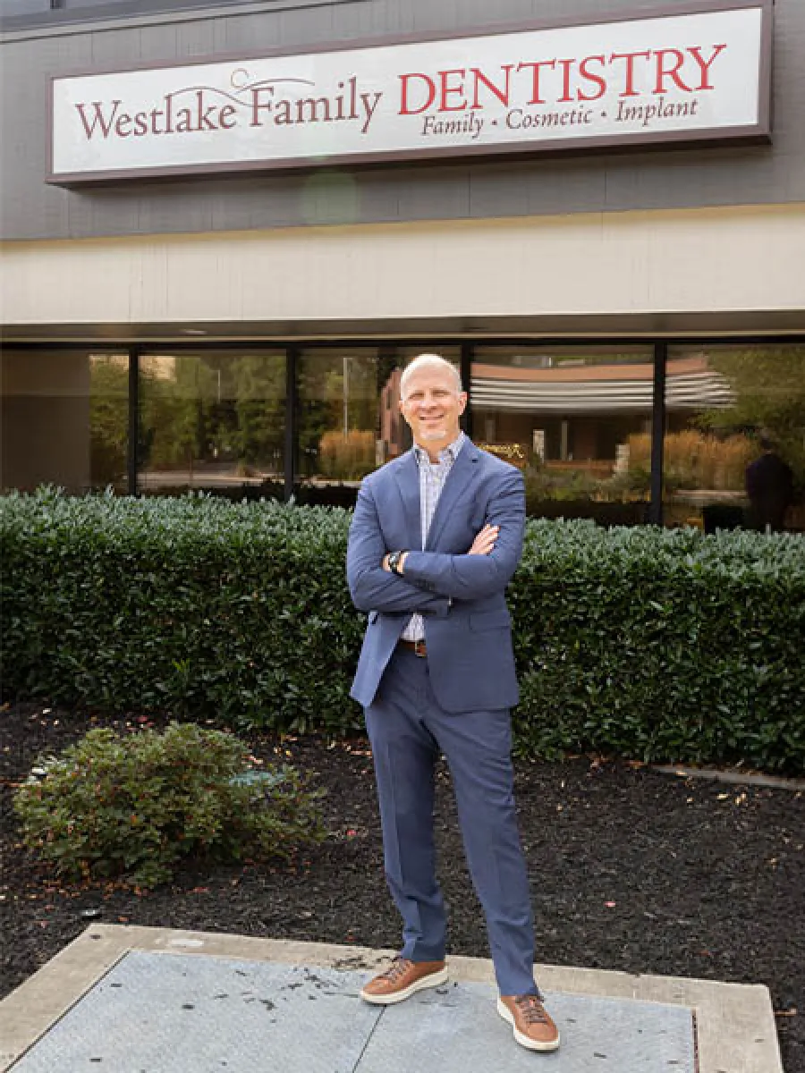 Man in blue suit standing with arms crossed outside Westlake Family Dentistry clinic with sign above