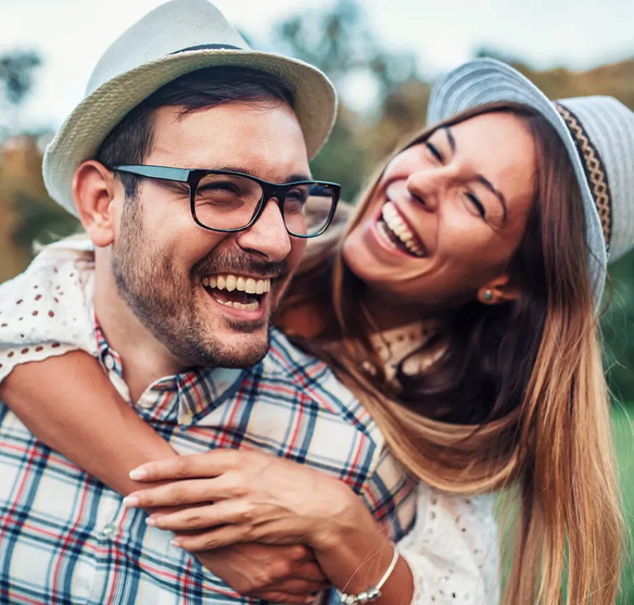 Happy young couple wearing hats laughing and enjoying a playful moment outdoors in nature.