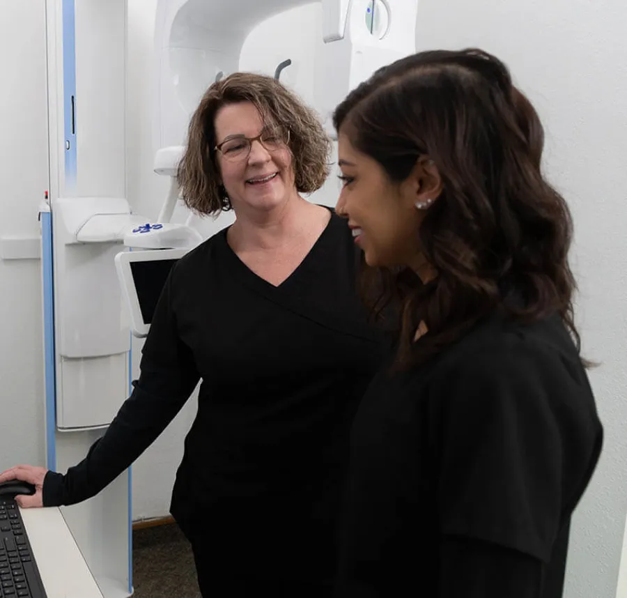 Female dental professionals in black uniforms discussing data by a dental imaging machine in clinic
