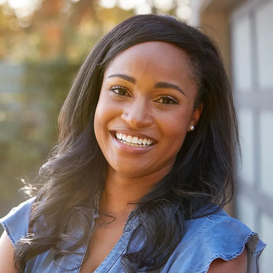 Smiling young woman with long black hair wearing a blue top outdoors in soft natural light