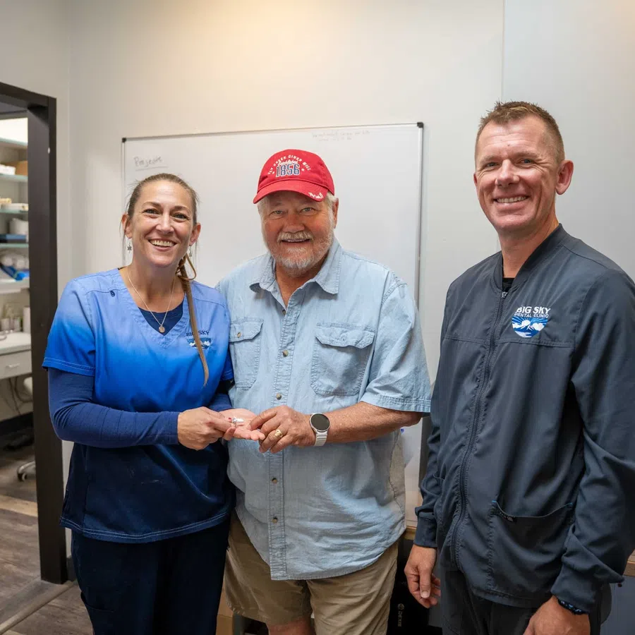 Smiling dental professionals with a male patient inside a dental clinic office setting.