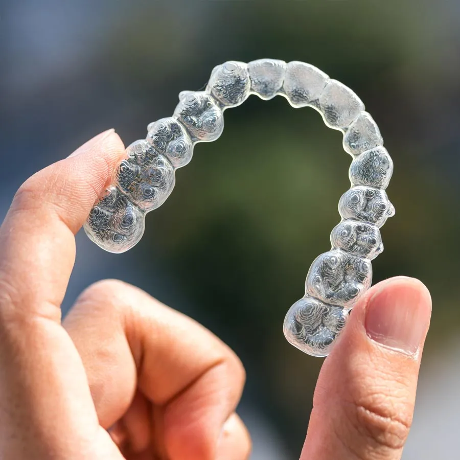 Person holding a clear orthodontic retainer against a blurred outdoor background.