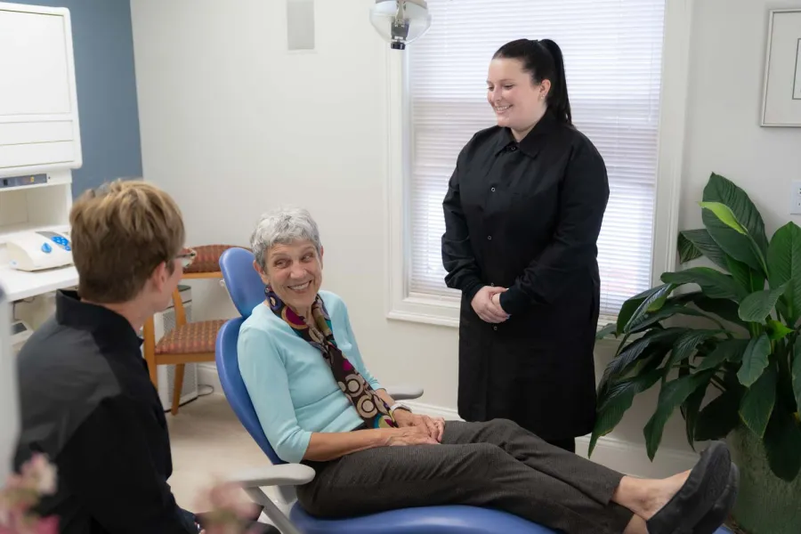 Senior woman smiling in dental chair while two dental professionals engage warmly with her