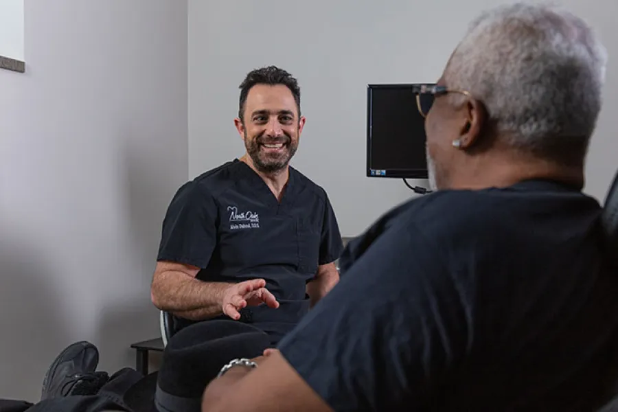 Dentist explaining digital dental scan results to a female patient using a touchscreen display in clinic.