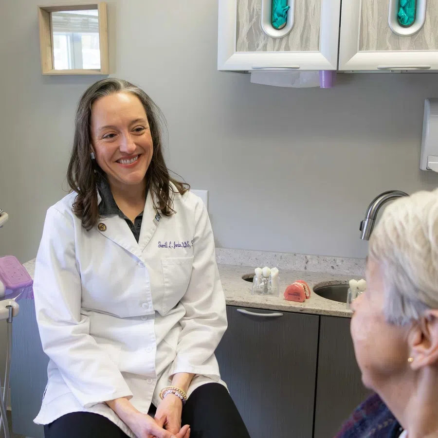 Female dentist in white coat smiling and consulting an elderly female patient in a dental office.
