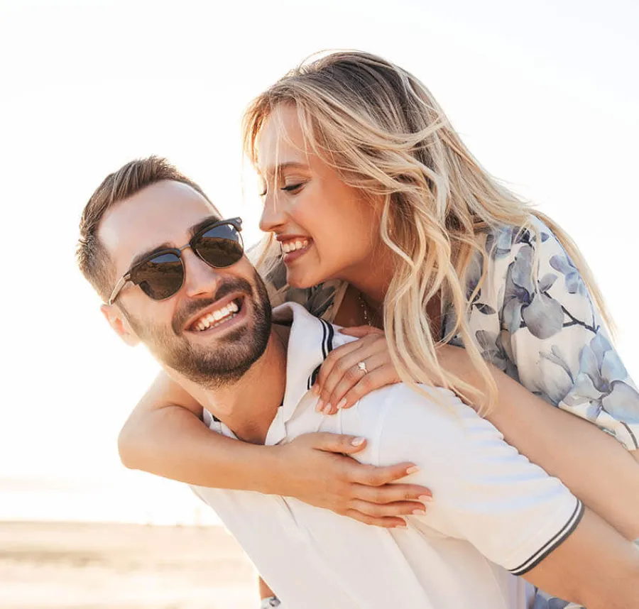 Happy couple enjoying a piggyback ride outdoors in bright sunlight, smiling and embracing each other.