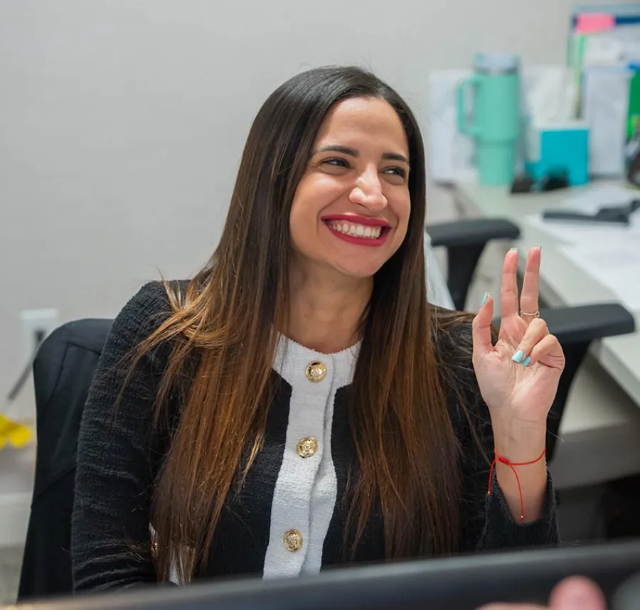 Smiling woman with long hair wearing a black and white outfit making a peace sign gesture indoors.