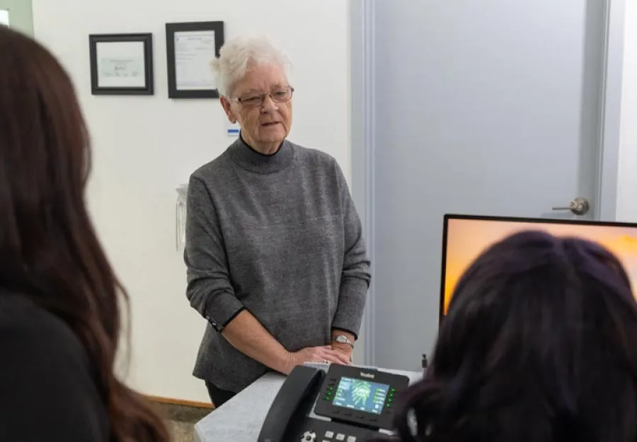 Elderly woman consulting with two medical professionals in a clinical office setting with diagnostic equipment.