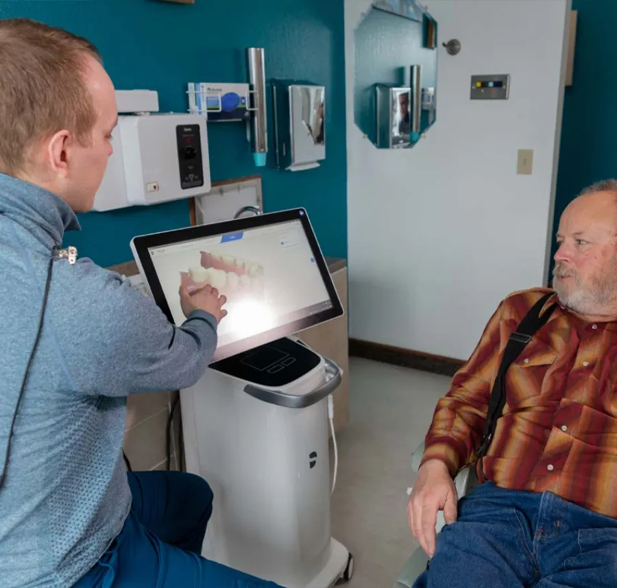Dental professional showing a 3D teeth model on a screen to an elderly male patient in a clinicroom.