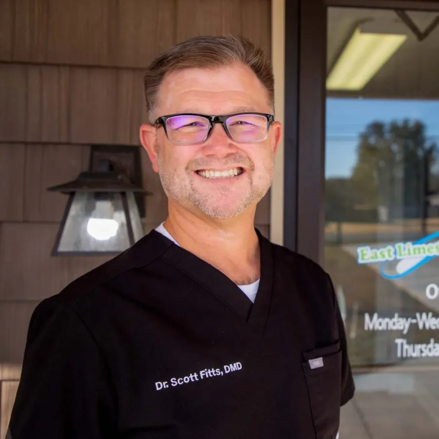 Smiling male dentist wearing glasses and black scrubs standing outside East Limestone Family Dental office.