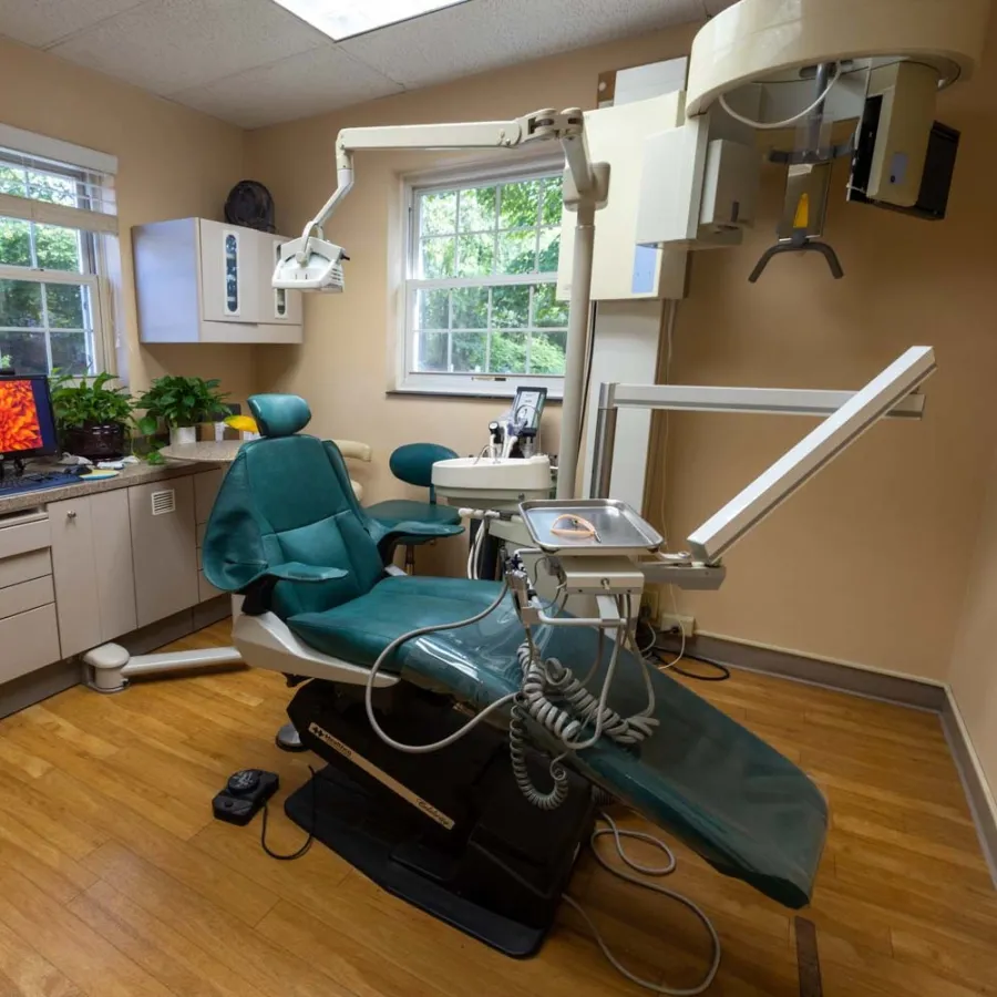 Modern dental office with green dental chair, equipment, computer, and natural light from windows.