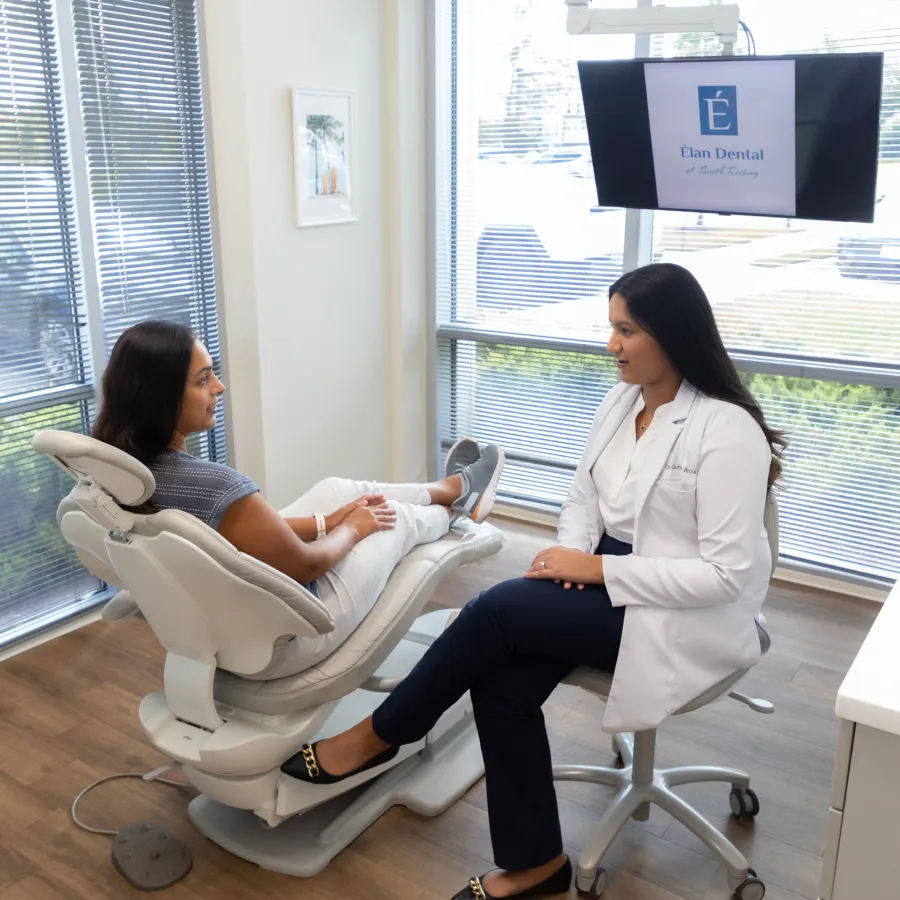 Dentist in white coat consulting with a patient seated in a dental chair in a bright office.