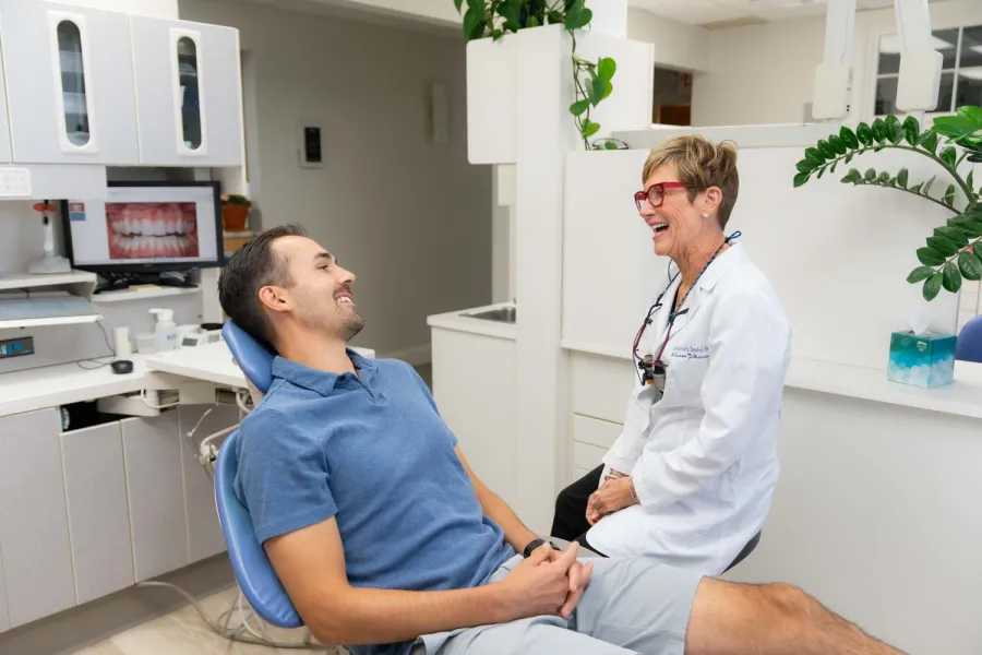 Dentist and male patient laughing during a dental checkup in a modern clinic with teeth x-ray on screen.