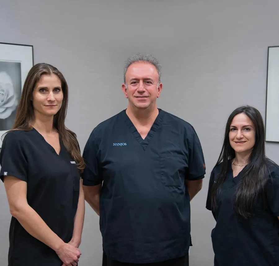 Three medical professionals in black scrubs standing in a clinic with framed floral artwork on the walls.
