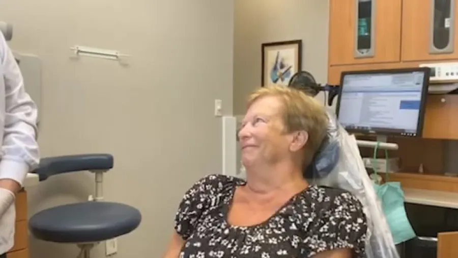 Smiling woman sitting in dental chair during a dental checkup with equipment and computer visible in the background