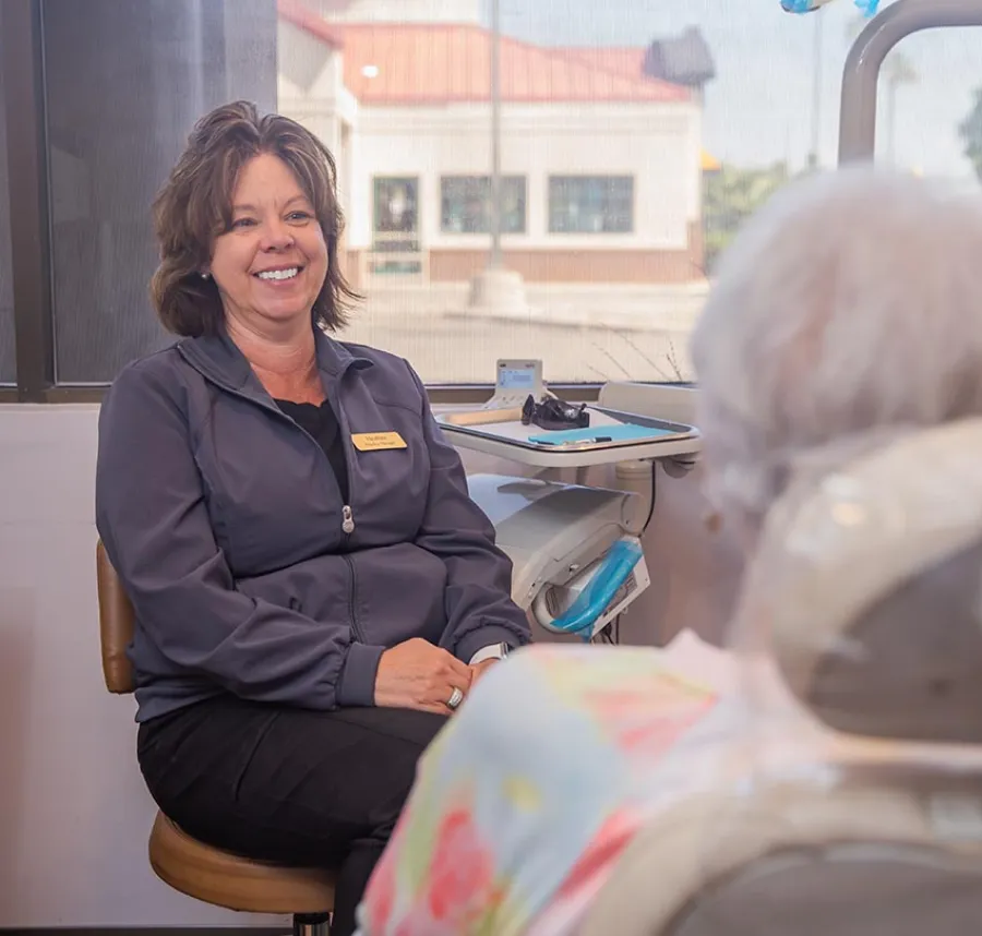 Smiling healthcare professional in uniform consulting with elderly patient in a bright clinic room.