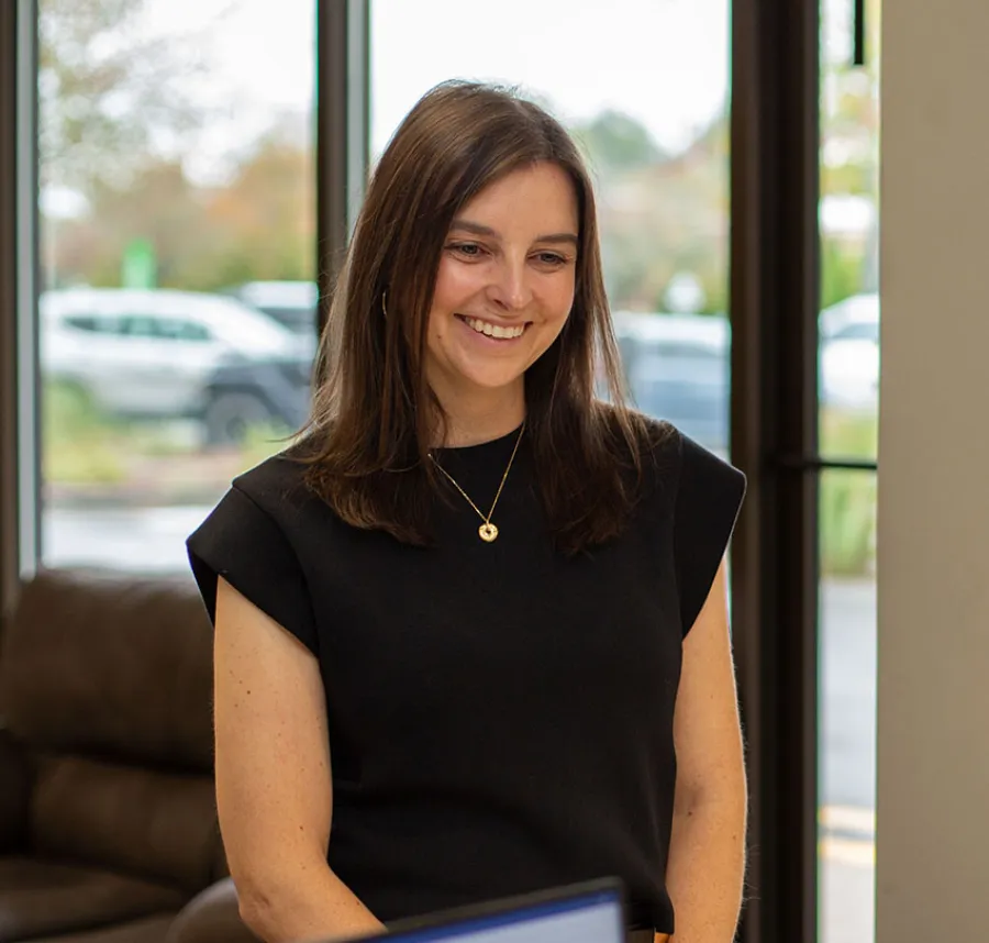 A woman smiling in a modern office environment with large windows and a cozy ambiance.