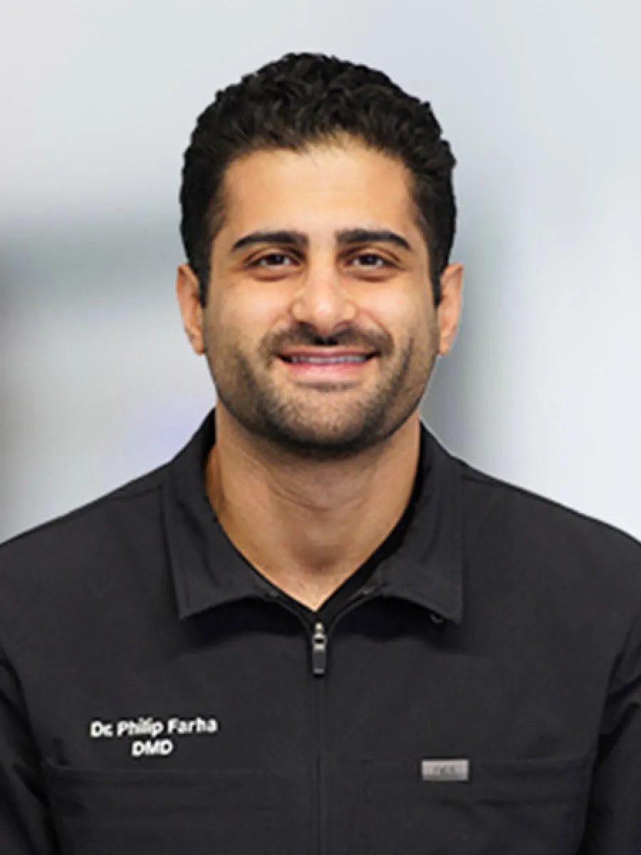 Smiling male dentist in black professional jacket with name badge.