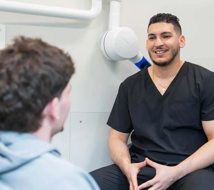 Smiling male healthcare professional in black scrubs consulting a patient in a clinical setting.