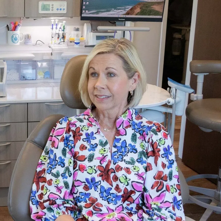 Woman in floral blouse sitting in dental chair consulting with dentist in modern clinic room.
