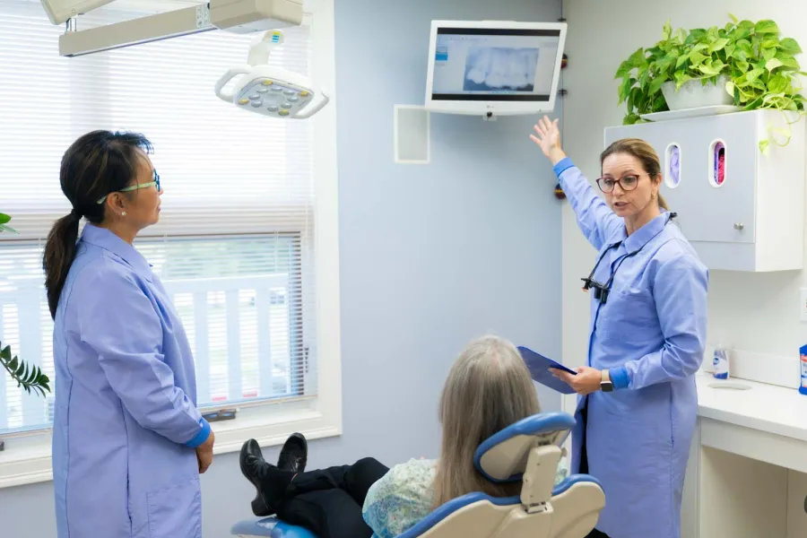 Dentist explaining dental X-ray results to a patient while another staff member observes in a bright clinic