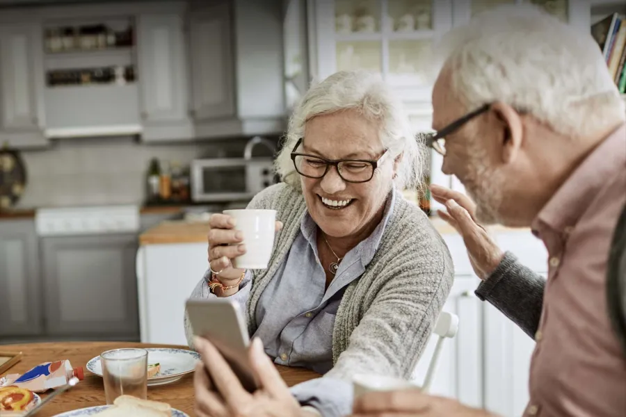 Happy seniors enjoying a moment together while looking at a smartphone in a cozy kitchen setting.