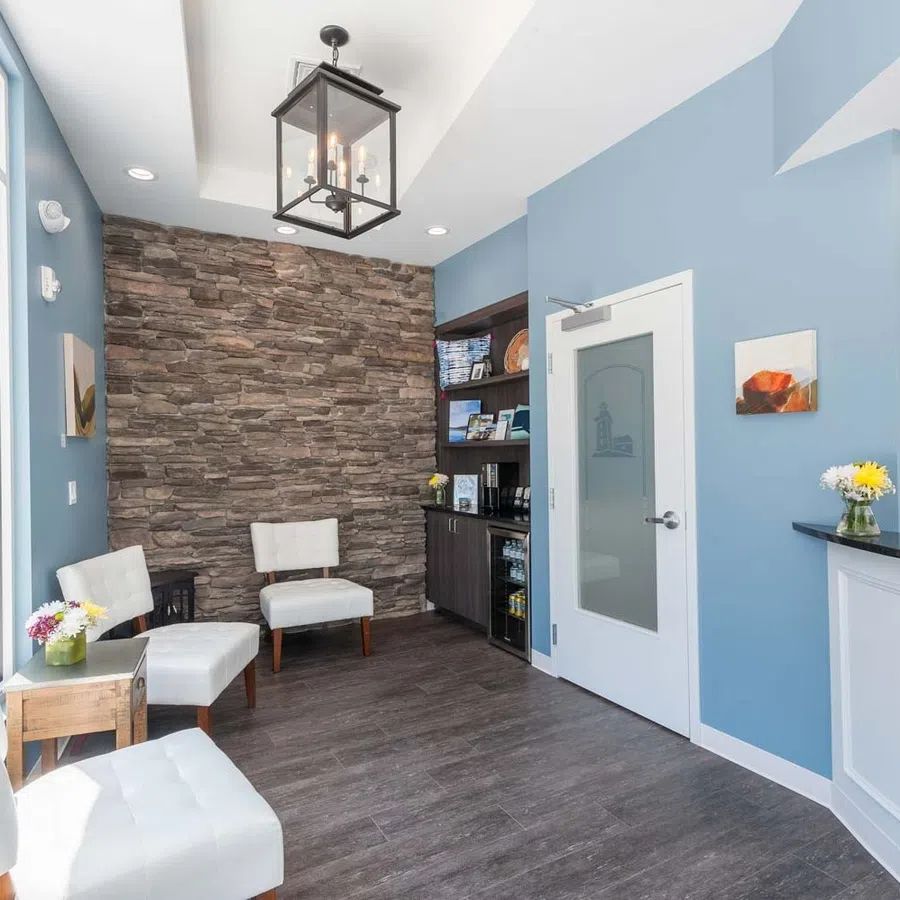 Bright waiting area with white chairs, stone accent wall, blue walls, and a window showing a sunny street outside