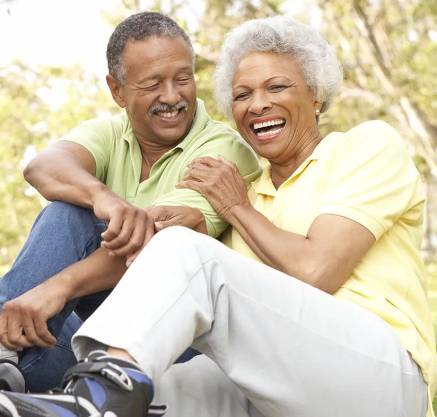 Happy older couple sitting outdoors laughing and enjoying a sunny day in casual clothes with rollerblades.