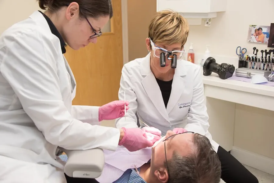 Dentists in white coats performing dental examination on male patient in clinic with dental tools.
