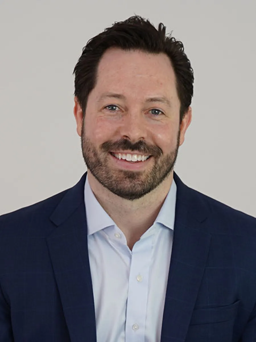 Smiling man in a blue suit with a light shirt, set against a plain background.