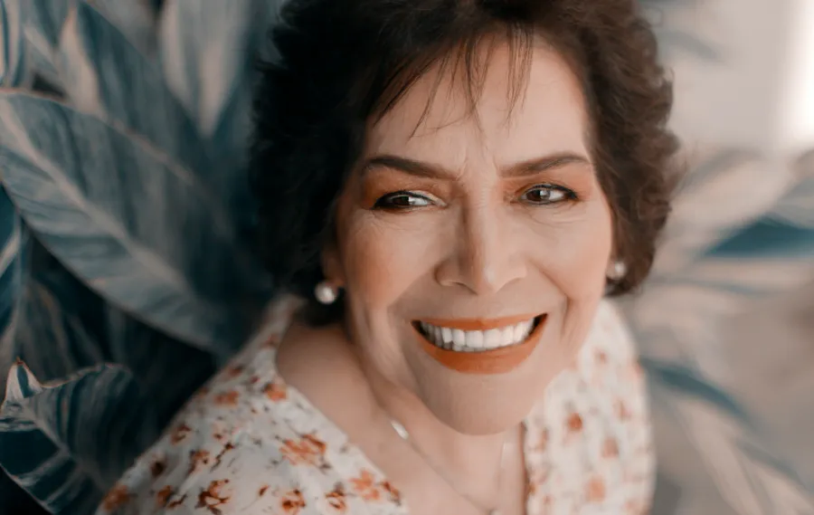 Close-up of a smiling mature woman with short hair wearing floral blouse and pearl earrings.