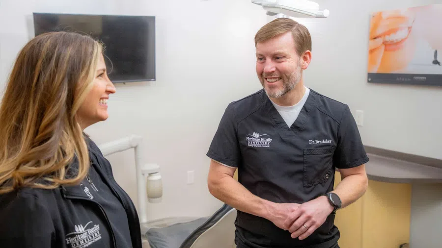 Two dental professionals smile and engage in conversation in a modern dental office setting.