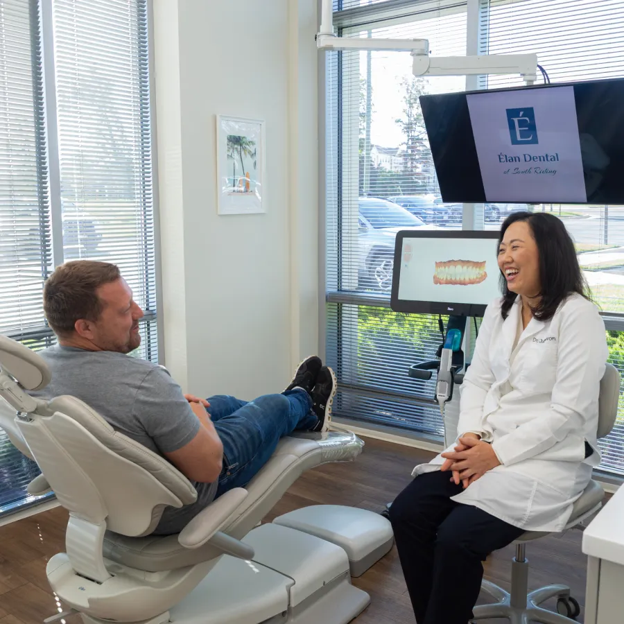 Dentist and patient smiling during a dental consultation in a bright, modern dental office with digital displays.