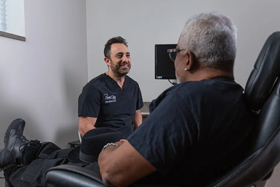 Doctor in black scrubs consulting a patient seated in a medical office chair in a clinical setting