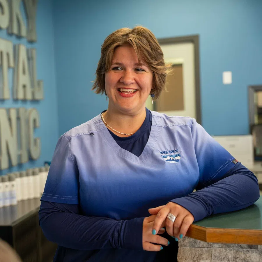 Smiling dental hygienist talking to a patient at a clinic reception desk with dental care products displayed.