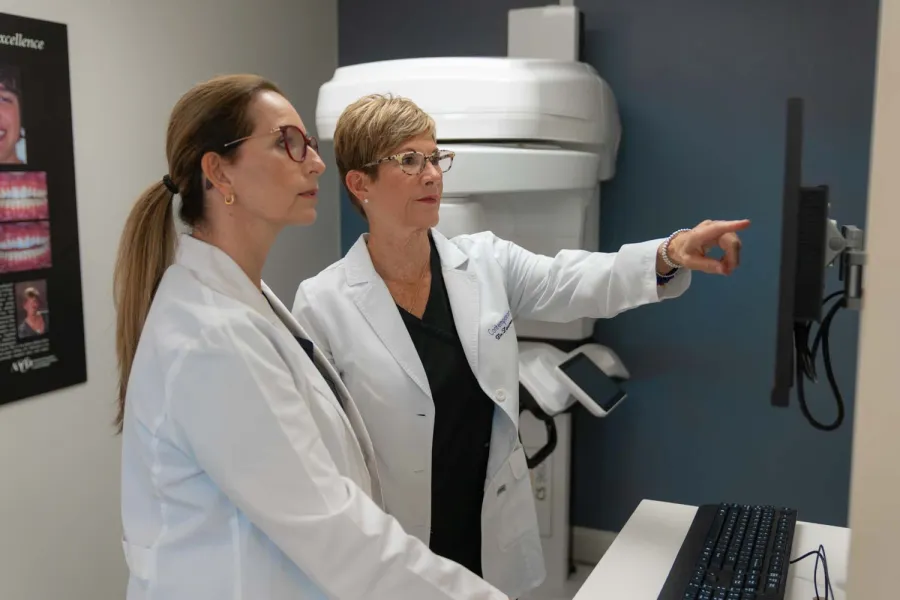 Two female doctors in white coats examining medical images on a computer screen in a clinic room.