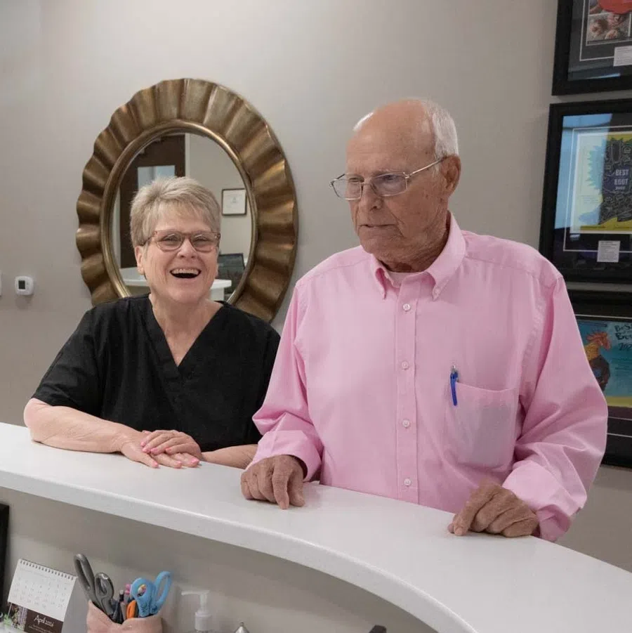 Receptionist assisting an elderly couple at the front desk in a modern medical or office setting.