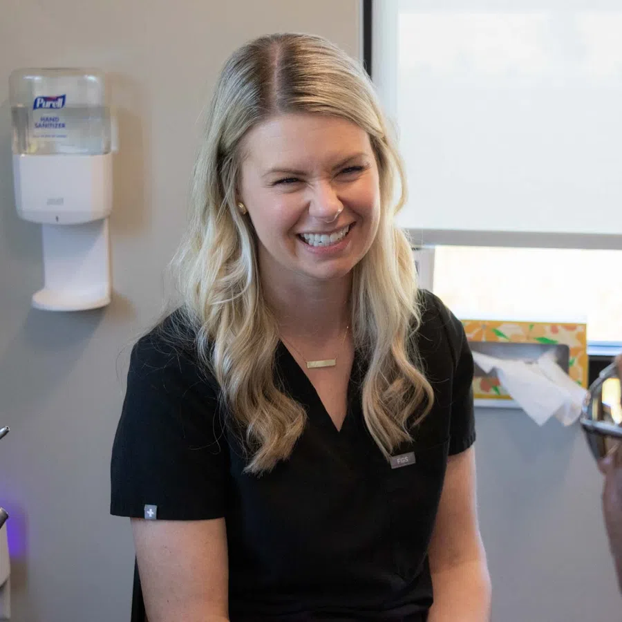 Smiling female dentist in black scrubs talking to a male patient in a bright dental clinic room.