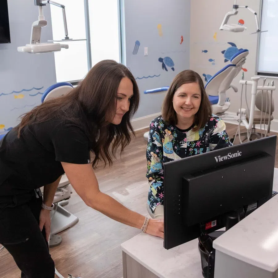 Two women reviewing information on a computer in a bright pediatric dental office with marine wall murals.