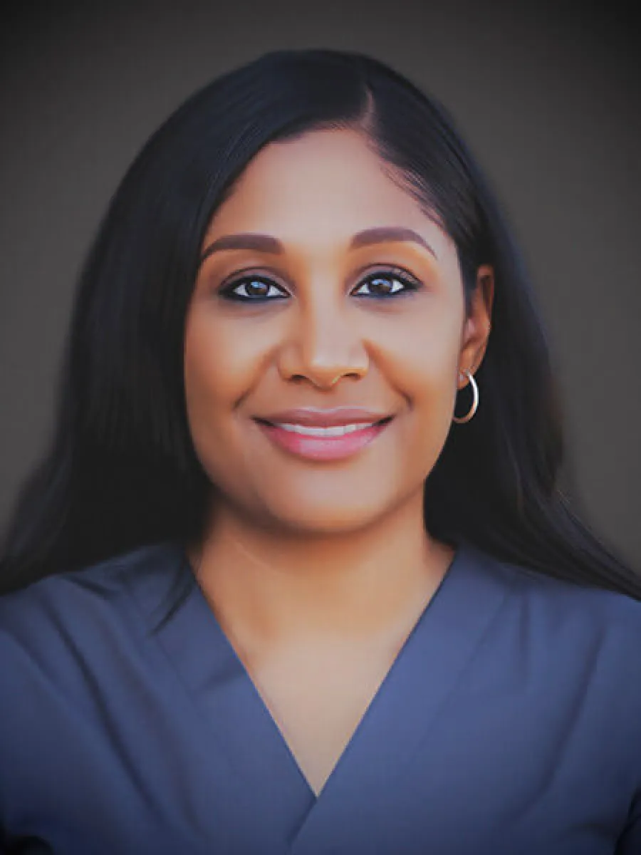 Smiling woman with long black hair wearing a blue top and hoop earrings on a dark background
