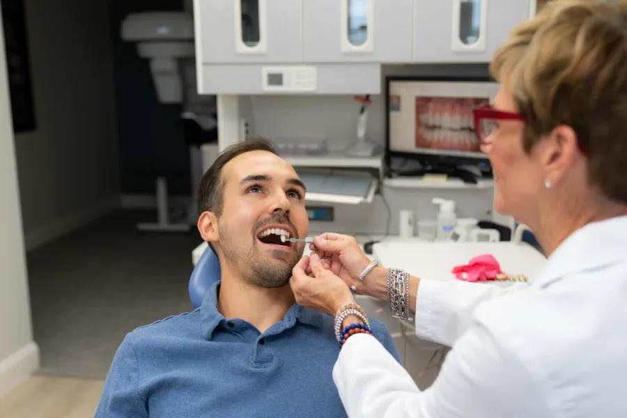 Dentist examining male patient's teeth using dental tools in a modern clinic setting.