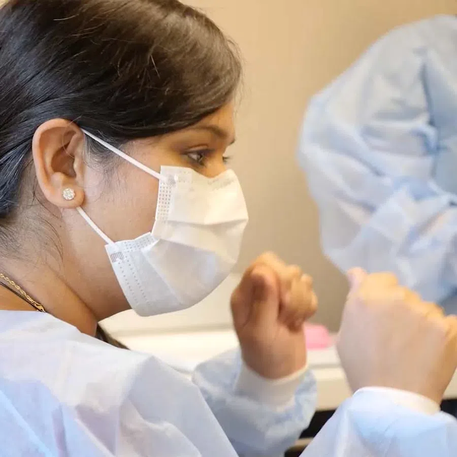 Healthcare professional wearing a mask and scrubs during a medical procedure in a clinical setting.