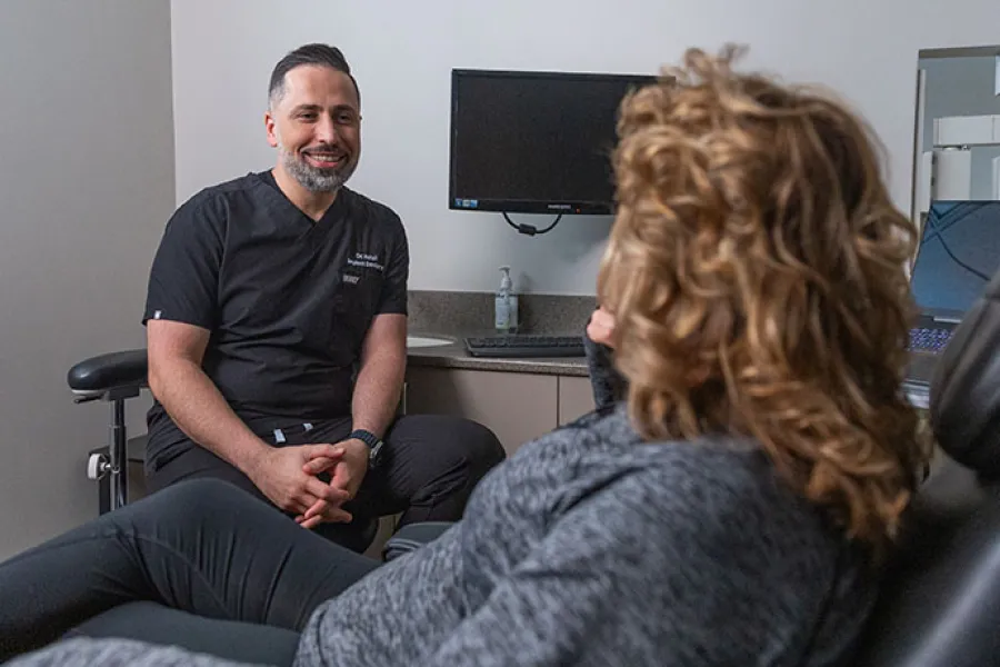 Male healthcare professional in black scrubs consulting with female patient in modern medical office.