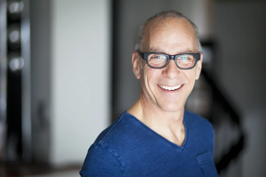 Smiling middle-aged man with glasses wearing a blue shirt in a softly lit indoor setting