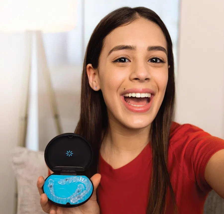 Smiling young woman showing clear dental aligners in a black case against a bright background